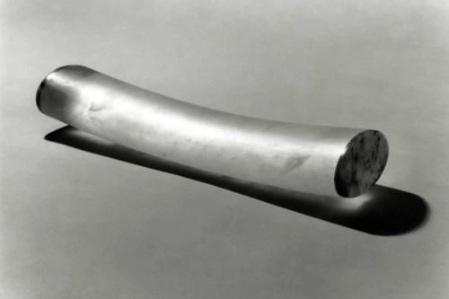 A translucent, slightly bent tube with dark ends on both sides rests on a gray floor