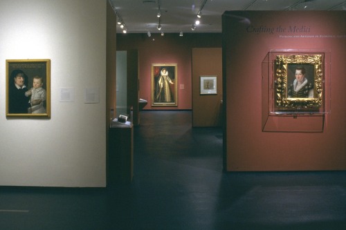 A gallery with maroon and white walls and a black floor with paintings in gold frames