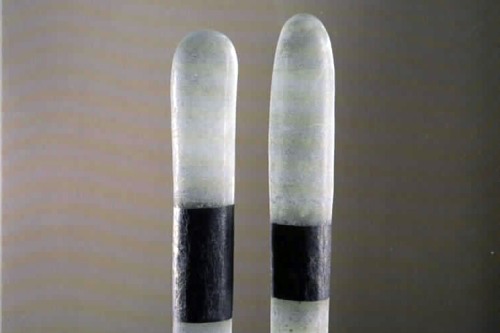 Two translucent glass poles with rounded tops and black bands stand on a glass brick on a wooden floor