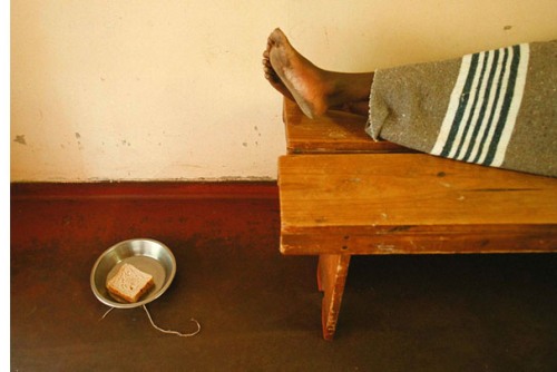 An image of a person lying on a board wrapped in a blanket with only the feet visible above a metal bowl with the slice of bread in it