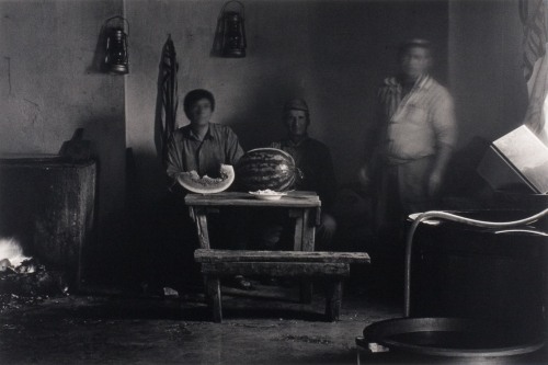 A blurry black and white photograph of three men before a large watermelon