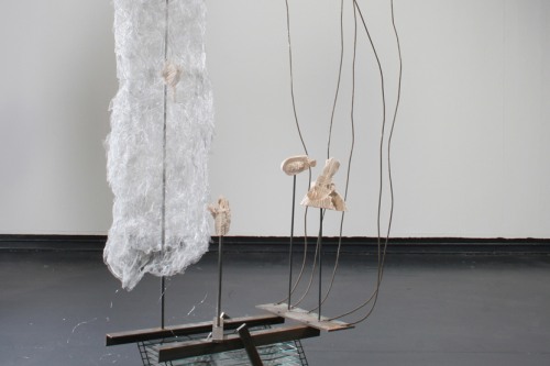 A sculpture of glass, wire, and other materials is in a gallery with a gray floor and white walls
