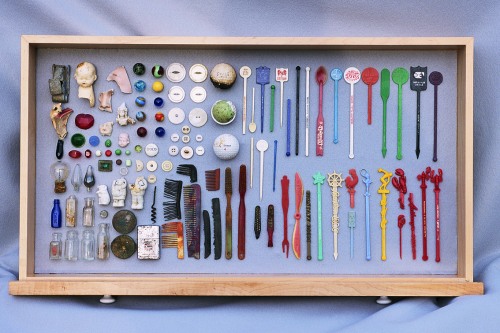 Knick knacks - buttons, pins, picks, combs, bulbs, marbles, shards and such - in a wooden cabinet box on top of blue fabric 