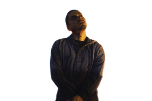 A man with his wrists crossed above his pelvis and feet together floats in a white space, reflecting a yellow light