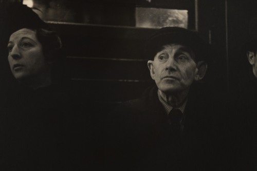 Three people wearing hats sit in a dark room by a window