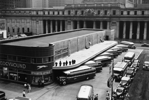 A black and white photograph of a bus stop in the city