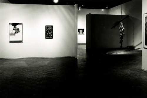 A black and white image of a gallery with sculpture and photographs 