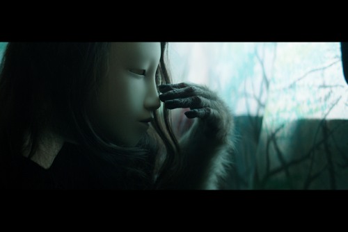 A woman with dark hair is wearing a mask and is being touched by what appears to be a monkey's hand