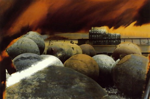 A collaged image of large metallic balls in front of a building in a fiery background