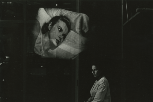 A black-and-white image with one woman shown at the bottom and another superimposed above; the first sits in the foreground staring away with a blank expression, and the second woman's head rests on pillows.