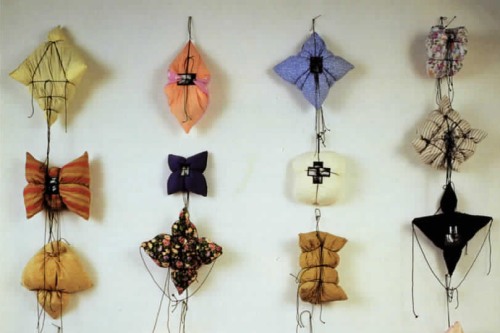 Uniquely shaped stuffed fabric objects hang off each other in a row by tied string