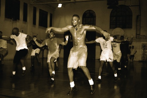 Sweating black men jump inside a gymnasium, practicing to fly