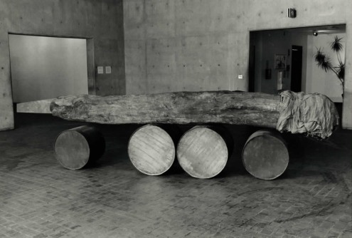 A long wooden object wrapped at one end is balanced on top of several barrels