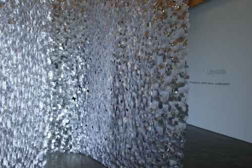 A large glass like curtain made of discs hangs in a gallery space 