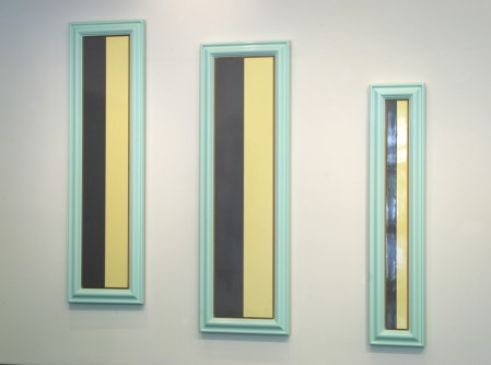 Photograph of three tall and thin framed almost identical paintings of a grey and a yellow stripe