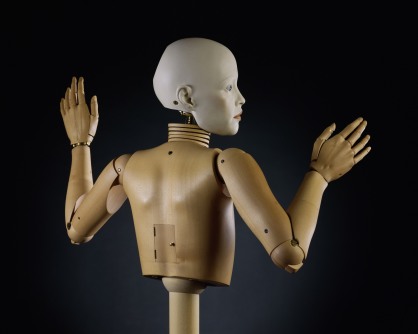 Sculpture of a realistic bald human face on top of a wooden mannequin torso