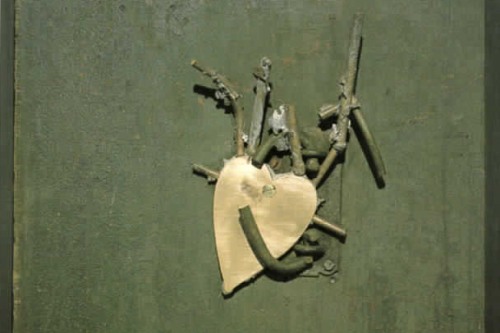 Sculpture of a metallic heart cutout surrounded by green industrial materials on a green wooden board